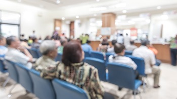 Um grupo de pessoas sentadas em cadeiras azuis numa sala de espera.